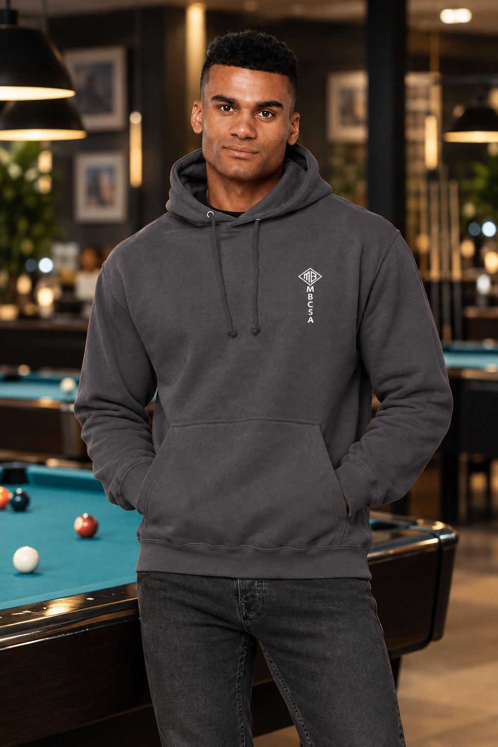 Model wearing the charcoal MBCSA hoodie in a pool hall